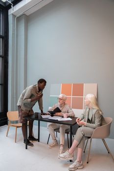 Group of diverse coworkers in stylish outfits gathering around table and discussing details of project in creative workplace